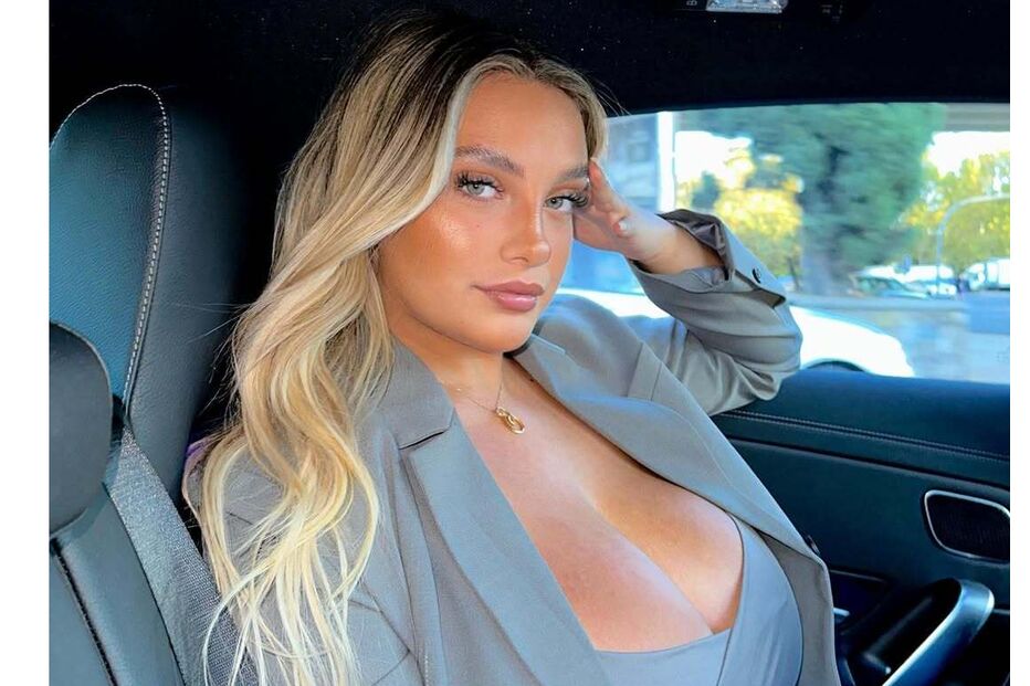 Mulher loira posa num carro com blazer cinzento