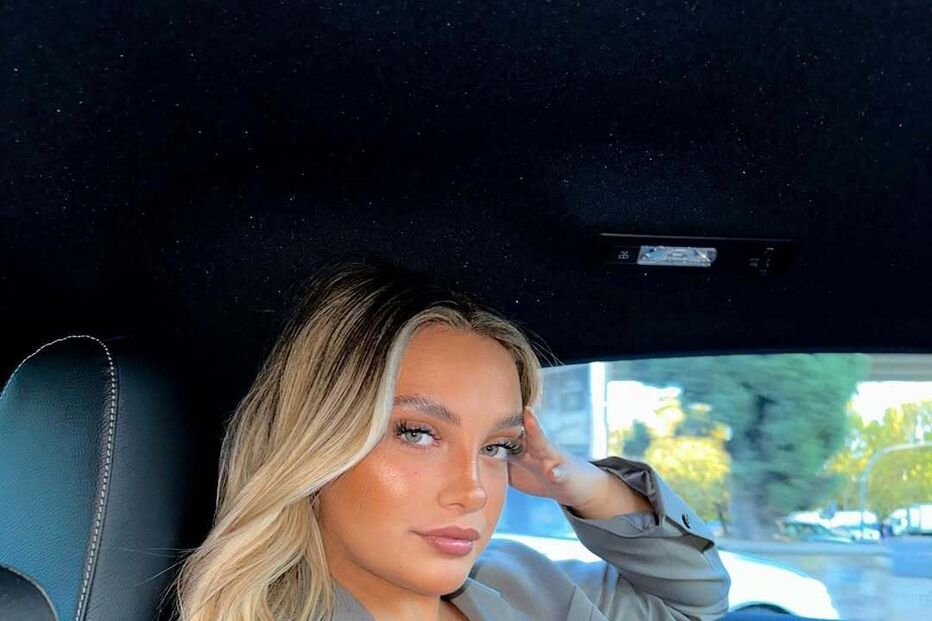 Mulher loira posa num carro com blazer cinzento