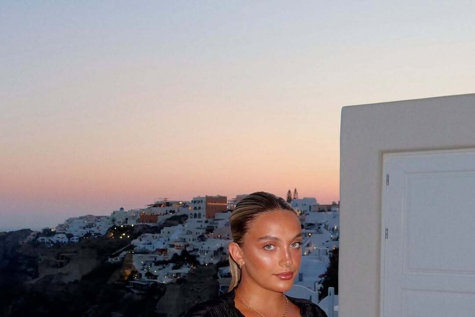 Mulher posa em Santorini com blusa preta e calças brancas