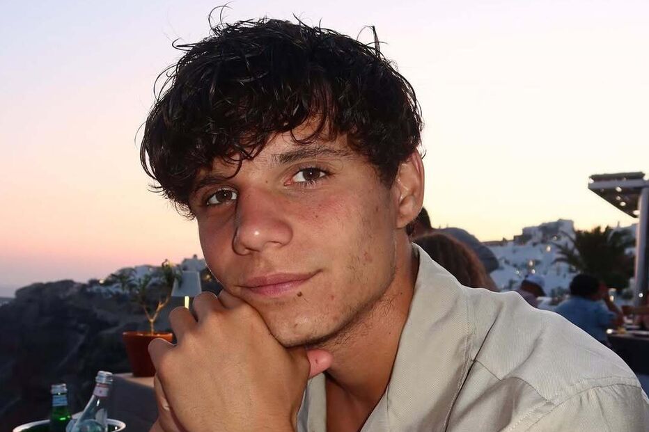 Homem posa num restaurante com vista para Santorini