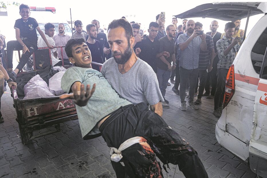 Homem carrega pessoa ferida para ambulância, sob o olhar de populares