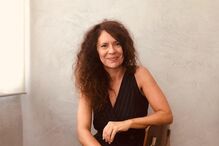 Mulher sorridente posa sentada numa cadeira com um macacão preto elegante