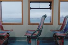 Interior de um ferry com bancos coloridos e vista para a água