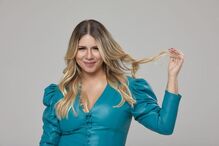 Marília Mendonça posa com blusa azul de mangas compridas e brinca com o cabelo loiro