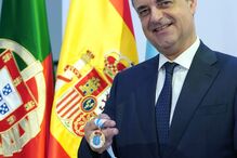 Um homem recebe condecoração com as bandeiras de Portugal e Espanha ao fundo