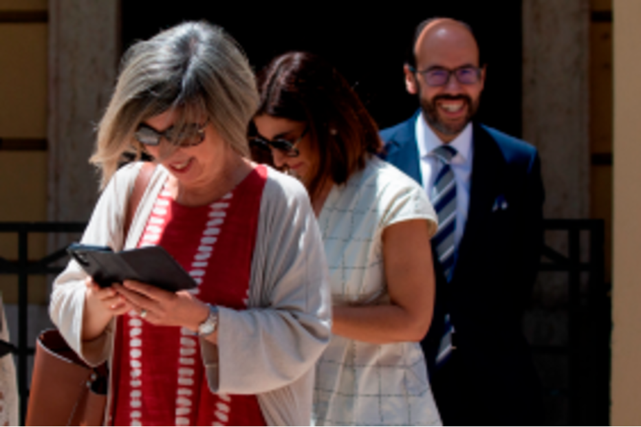 Pessoas caminham juntas num dia ensolarado, uma delas consulta o telemóvel