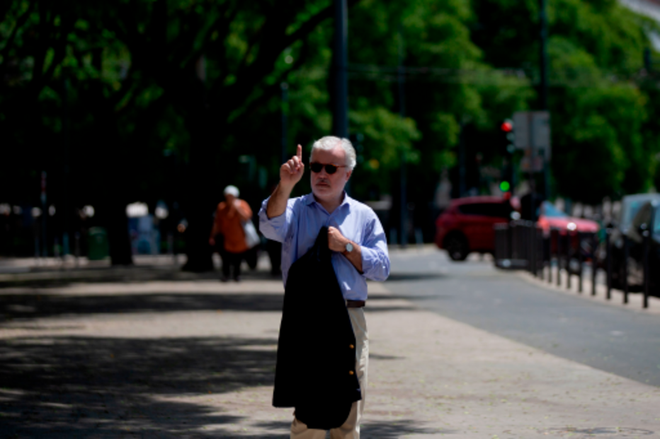Homem gesticula na rua, com árvores e carros como fundo em Lisboa