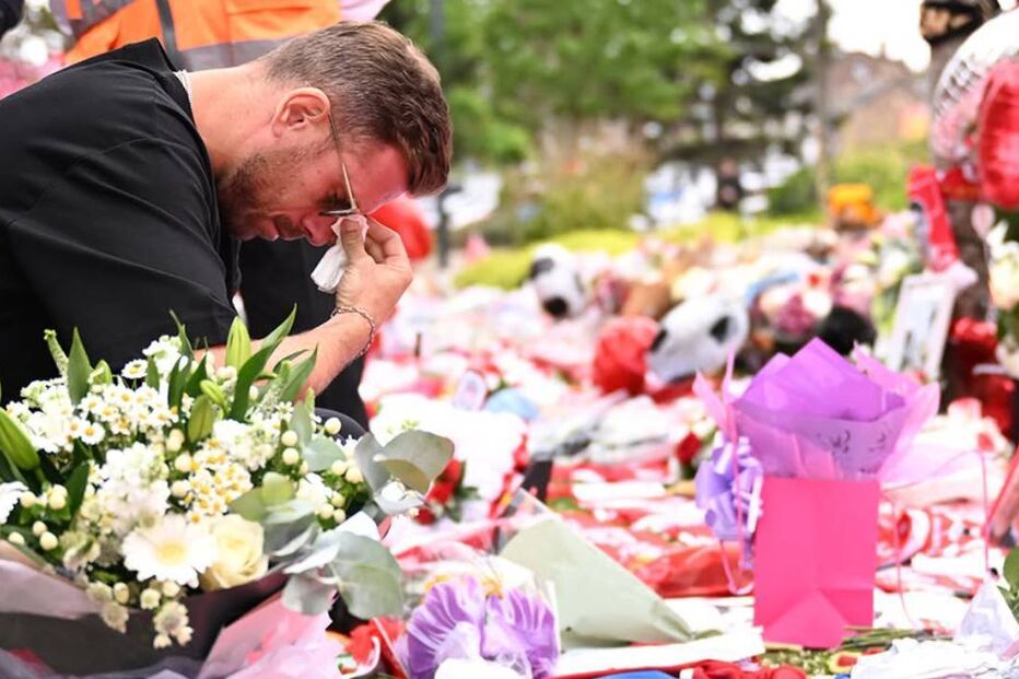 Homem emocionado presta homenagem num memorial cheio de flores e presentes
