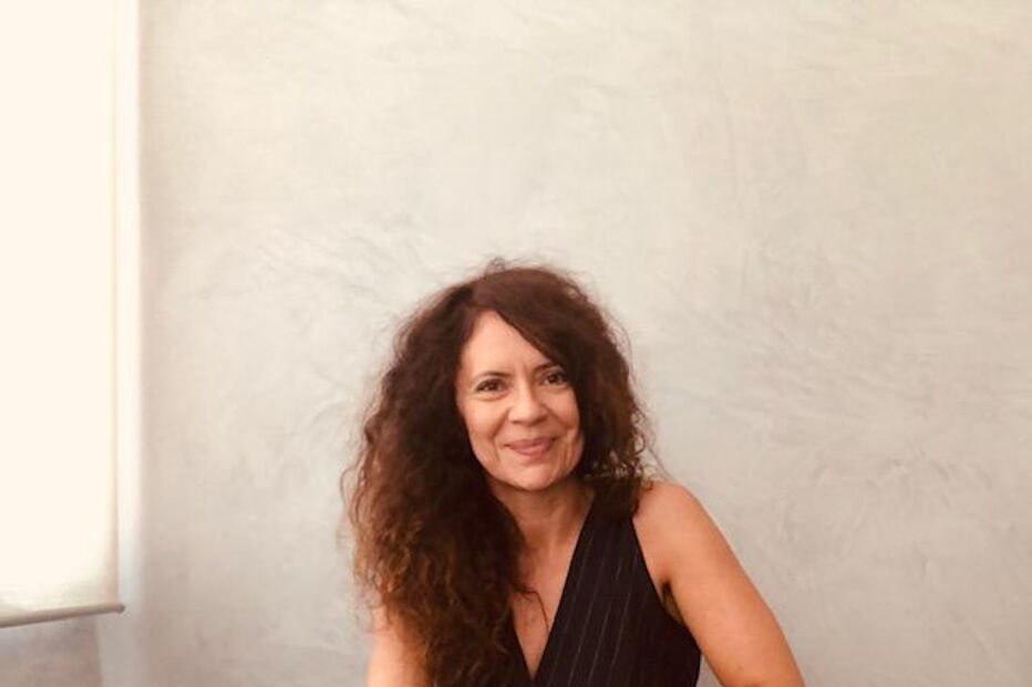 Mulher sorridente posa sentada numa cadeira com um macacão preto elegante