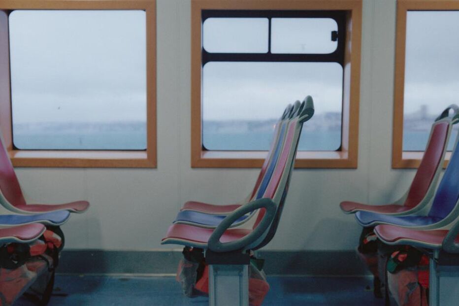 Interior de um ferry com bancos coloridos e vista para a água