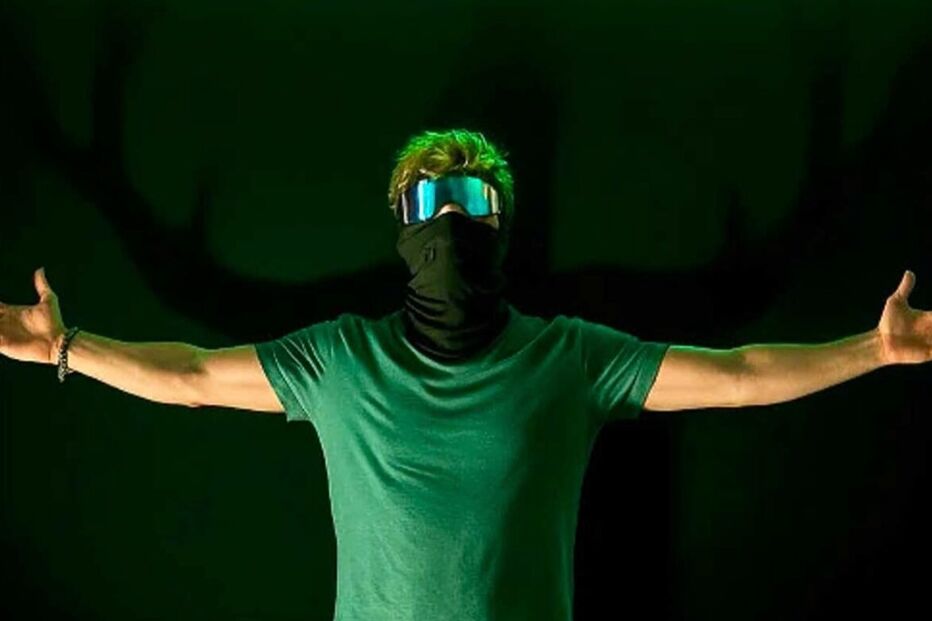 DJ Vyntrix atua com máscara e óculos futuristas num palco com luzes verdes.
