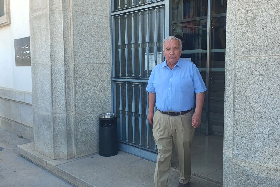 Homem de camisa azul e calças bege em frente a edifício