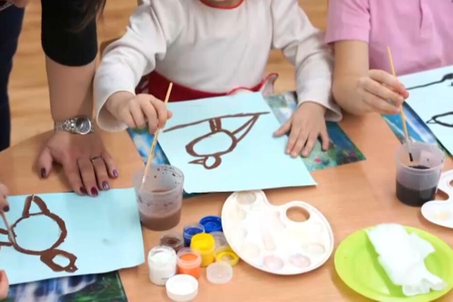 Crianças pintam desenhos em papel numa atividade criativa