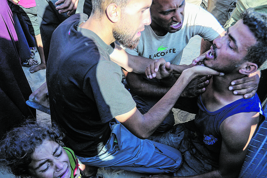 Gaza: Homem ferido recebe auxílio enquanto criança chora, após incidente em centro de distribuição