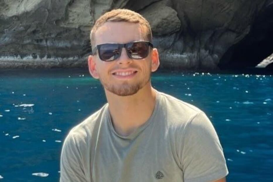 Homem sorri num barco com gruta e cascata em fundo azul