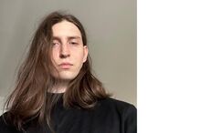 Um homem com cabelo comprido e camisa preta posa para a câmara