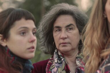 Três mulheres posam juntas, com foco na do meio, em ambiente natural