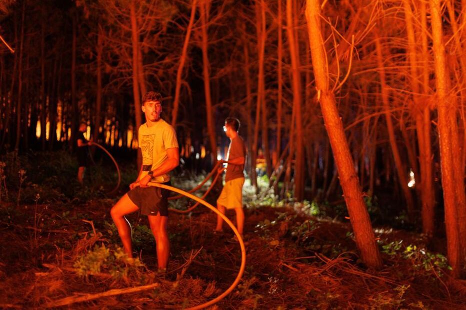 Voluntários combatem incêndio florestal com mangueiras durante a noite