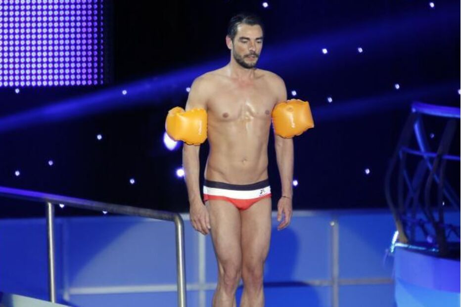 Homem de tronco nu e com braçadeiras na prancha de mergulho