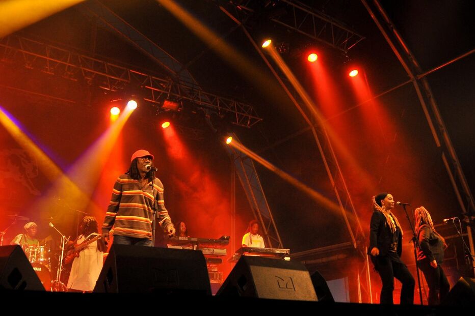 Banda atua num palco iluminado com focos coloridos durante concerto