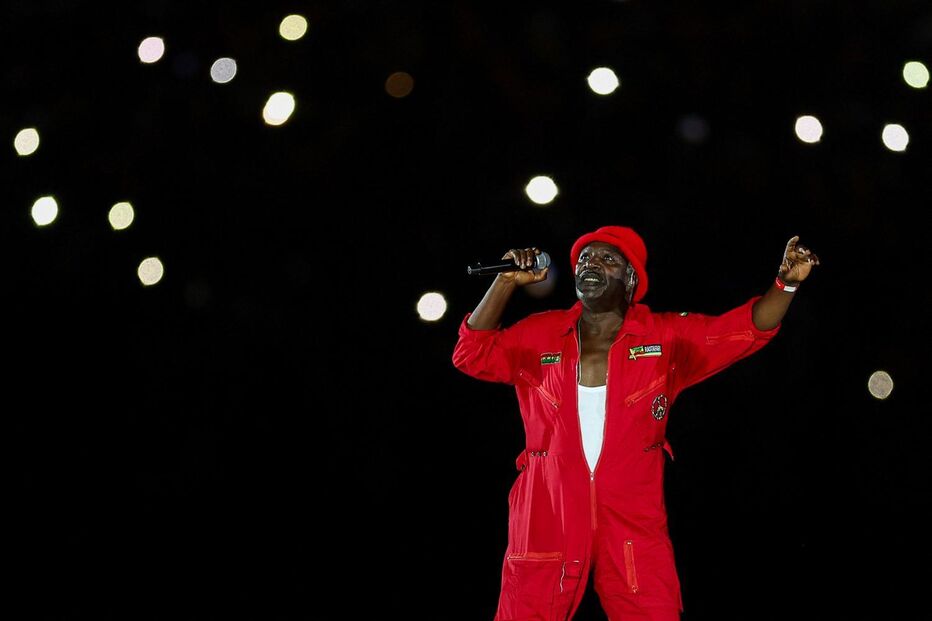 Artista atua no palco com microfone e fato vermelho