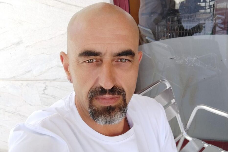 Homem careca com barba grisalha e tatuagem no braço posa para foto