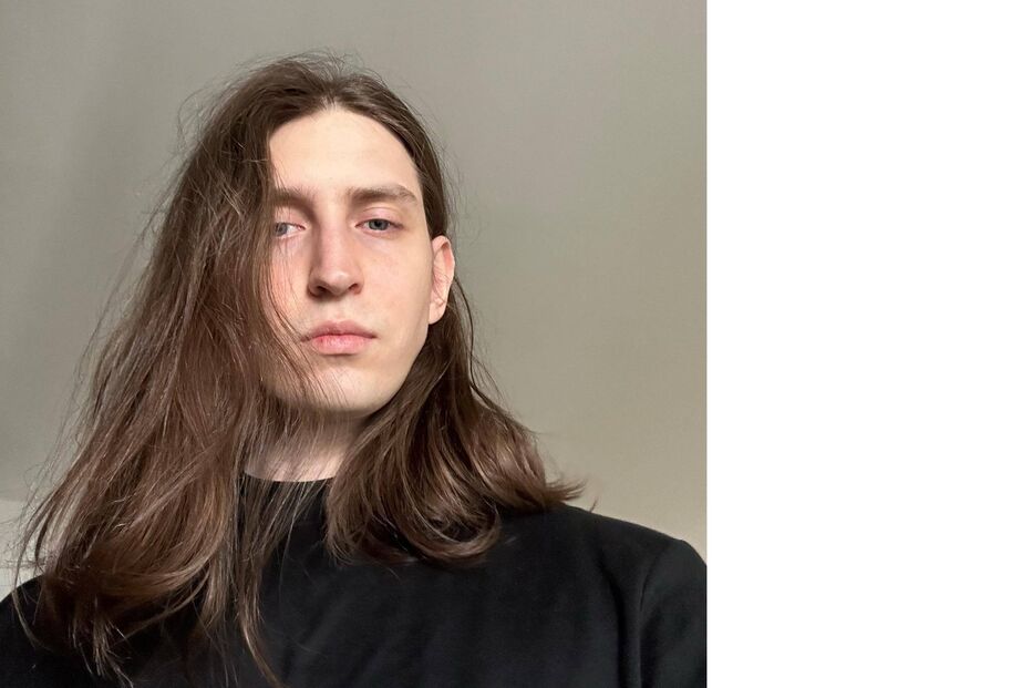 Um homem com cabelo comprido e camisa preta posa para a câmara