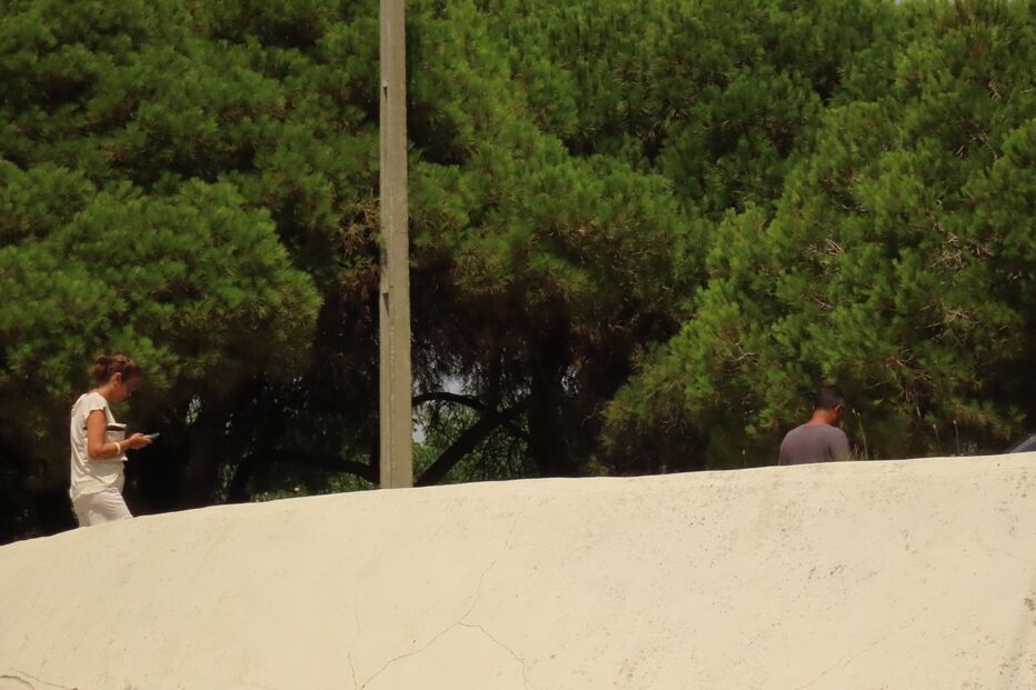 Pessoas caminham perto de uma parede sob árvores