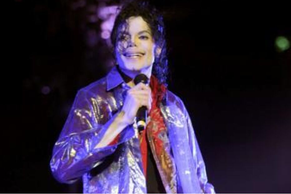 Michael Jackson surge sorridente num palco, segurando um microfone