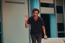 Ator em cena gesticula com a mão e segura objeto