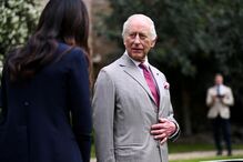 O rei Carlos III encontra-se com uma mulher num jardim.
