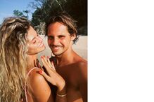 Um casal sorri numa praia tropical, com destaque para o anel da mulher