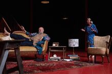 Num palco, dois atores contracenam num cenário interior
