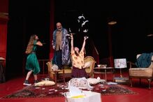 Num palco, atores contracenam com almofadas e penas brancas