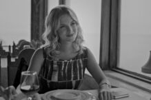 Mulher sorri à mesa perto da janela num restaurante