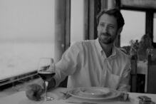 Homem à mesa com copo de vinho e vista para o mar