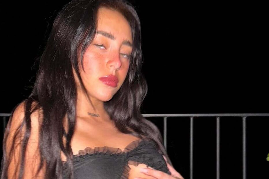 Mulher de vestido preto posa com mão no peito