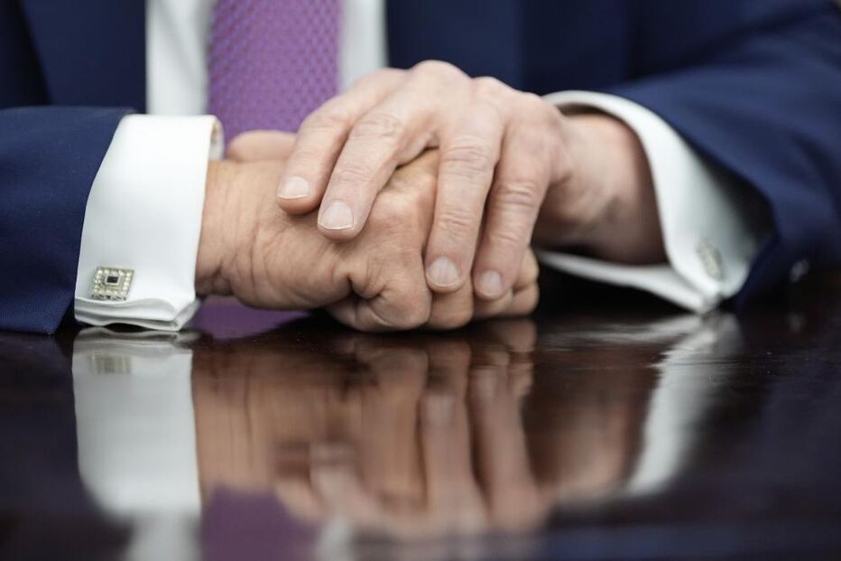 Mãos de Donald Trump em cima de uma mesa com reflexo