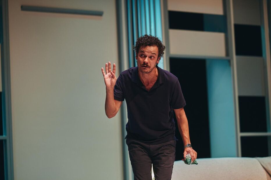 Ator em cena gesticula com a mão e segura objeto