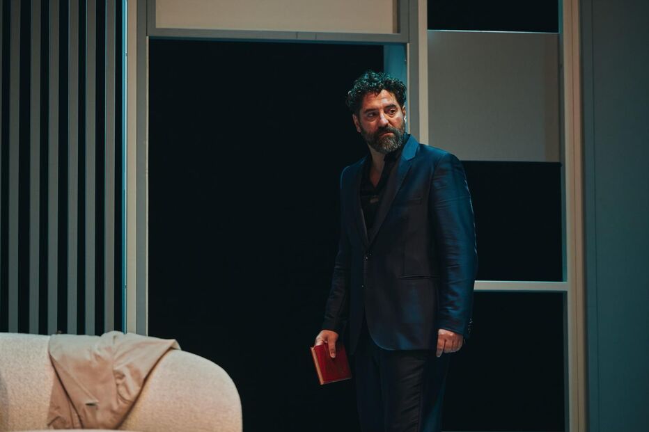 Homem de fato segura livro num cenário teatral