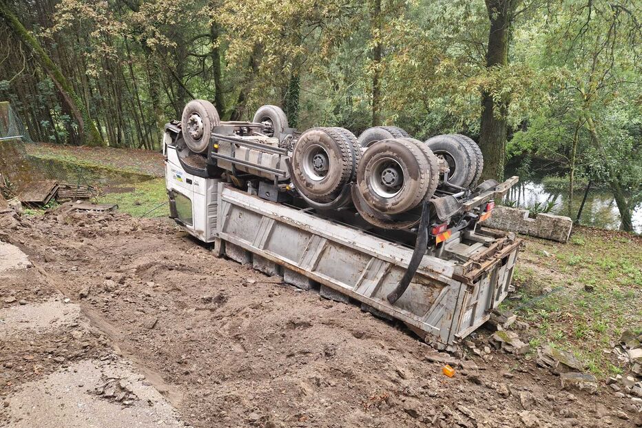 Camião tombado numa zona de terra, perto de árvores e água