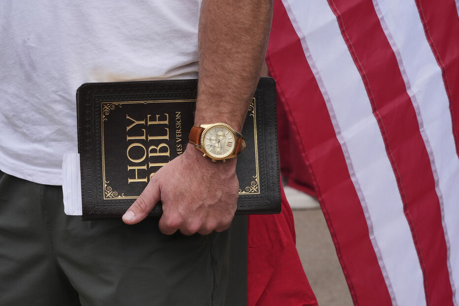 Homem segura bíblia com bandeira americana, durante cerimónia de despedida de Charlie Kirk