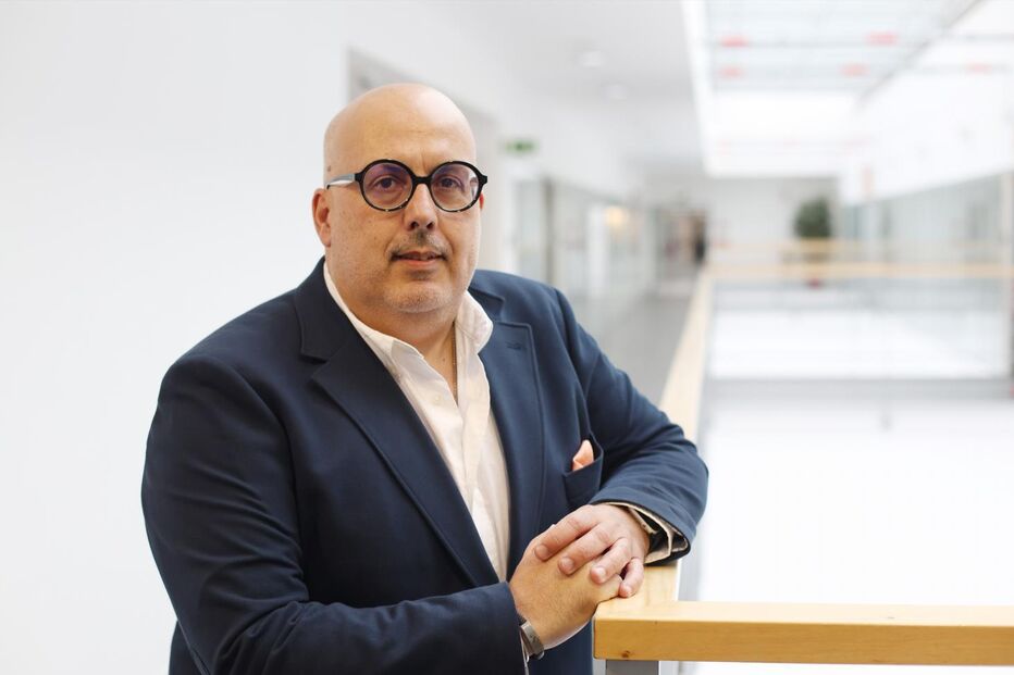 Homem de óculos com blazer posa para a câmara