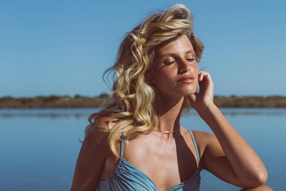 Mulher de fato de banho azul relaxa ao sol perto da água