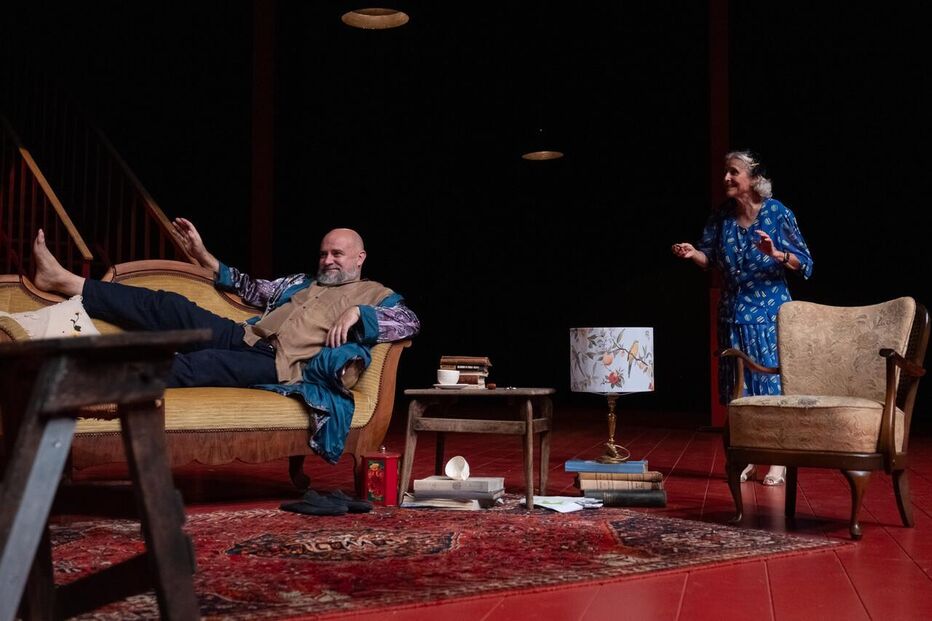 Num palco, dois atores contracenam num cenário interior