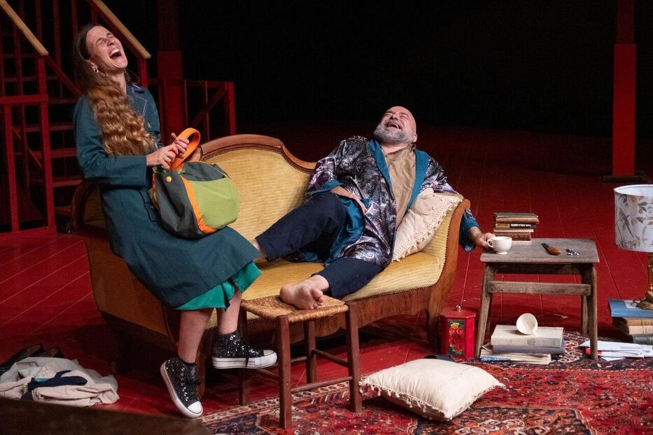 Num palco, dois atores partilham gargalhadas num cenário teatral