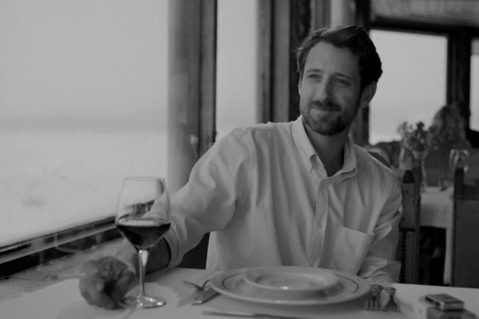 Homem à mesa com copo de vinho e vista para o mar