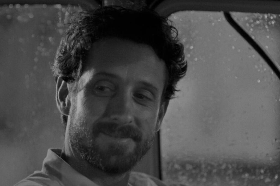 Homem sorri enquanto conduz num dia chuvoso