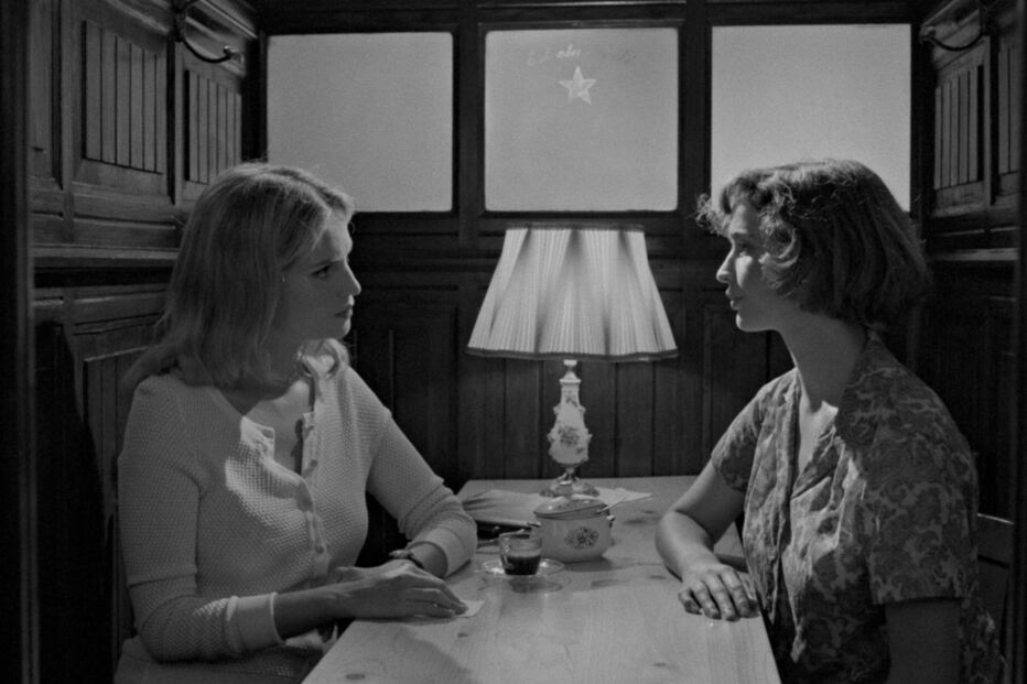 Duas mulheres frente a frente numa mesa, em espaço fechado com luz fraca