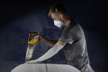 Homem corta prancha de surf com serra Stanley, usa máscara e auscultadores